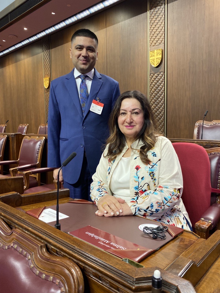Shoaib Rizvi stands next to and Senator Salma Ataullahjan who is sat with her hands together on the desk