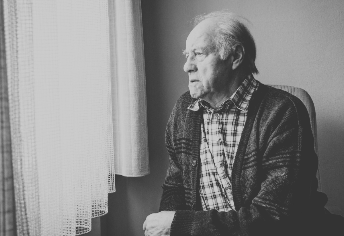 An older man stares out of a window looking melancholy